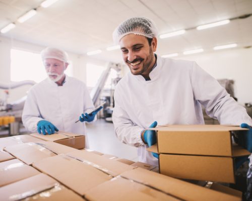 Two male colleagues i sterile clothes preparing boxes with products for transport. Standing in bright room or warehouse and counting package. Two male colleagues i sterile clothes preparing boxes with products for transport. Standing in bright room or warehouse and counting package.